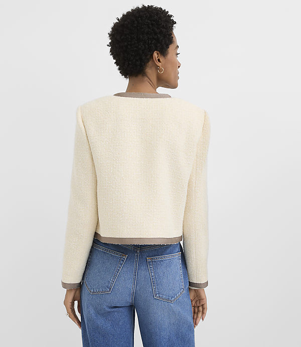 A woman in a cream tweed jacket and blue jeans stands against a plain white background.