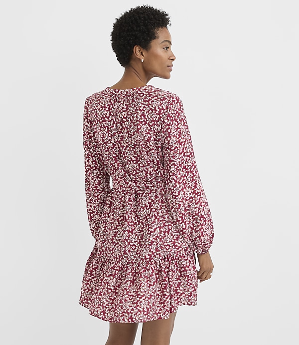 A woman in a floral print dress stands against a plain white background.