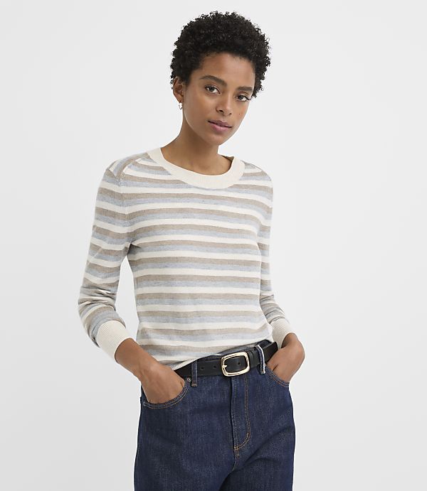 A woman in a striped sweater and dark jeans stands against a plain white background.