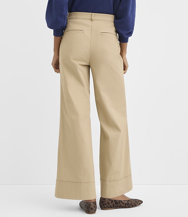 A person wearing tan wide-leg pants and leopard print flats stands against a plain white background.