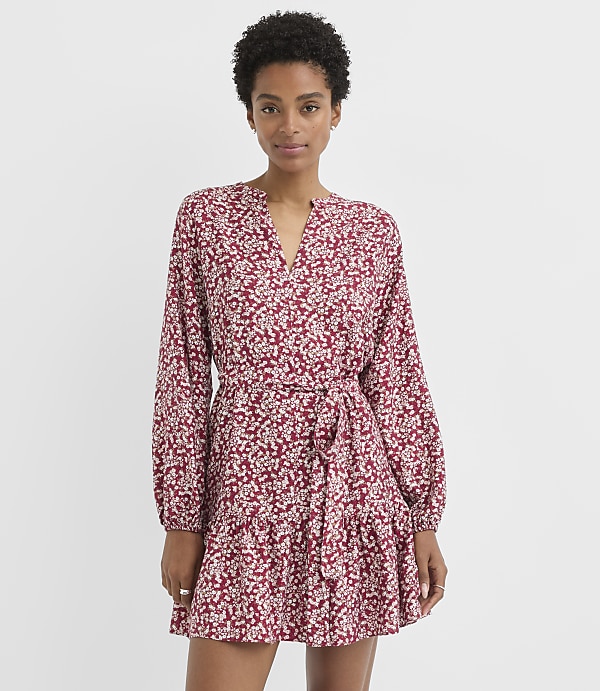 A woman in a floral print dress stands against a plain white background.