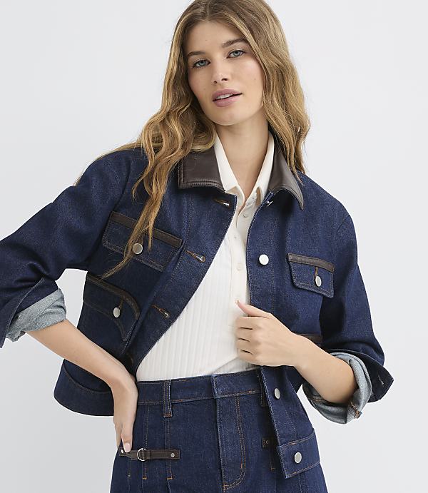 A woman in a denim jacket and skirt stands against a plain white background.