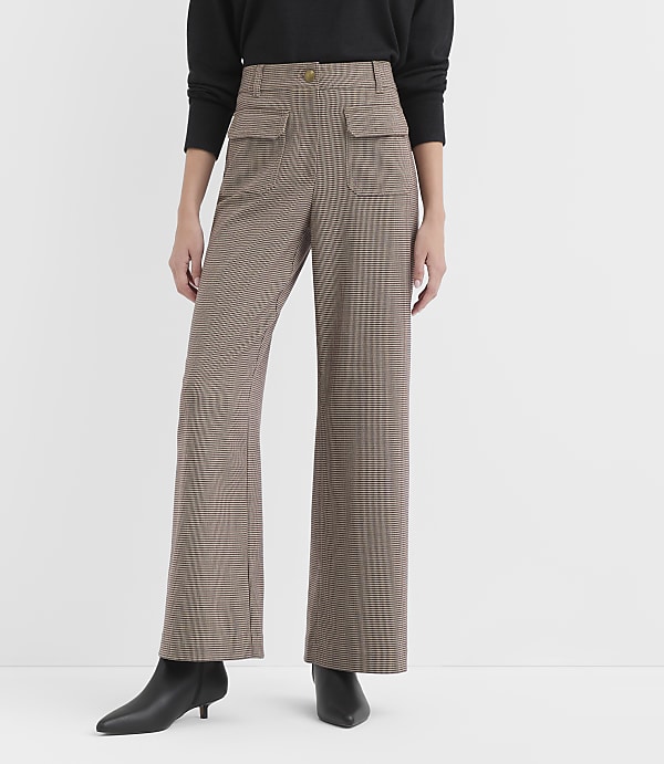 A person stands in front of a plain white background, wearing high-waisted, wide-leg plaid pants and black heeled boots.