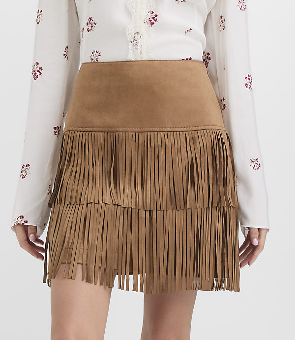 A model wears a brown suede fringed skirt over a white floral blouse against a plain white background.