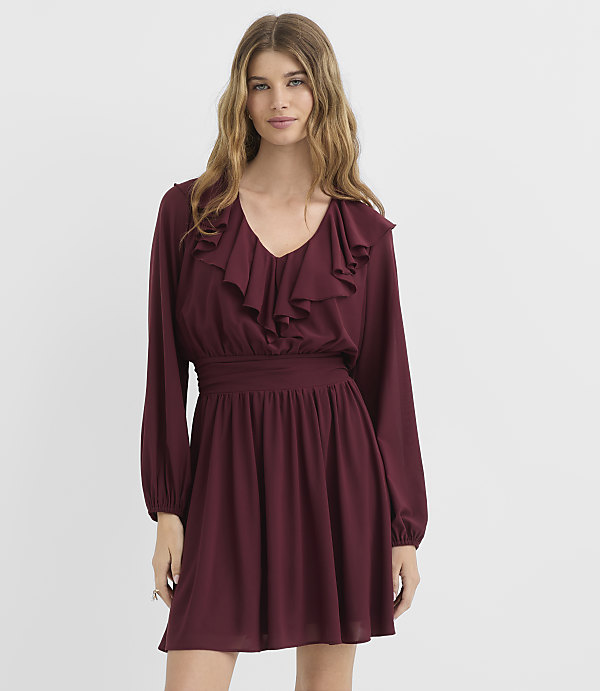 A woman in a burgundy ruffled dress stands against a plain white background.