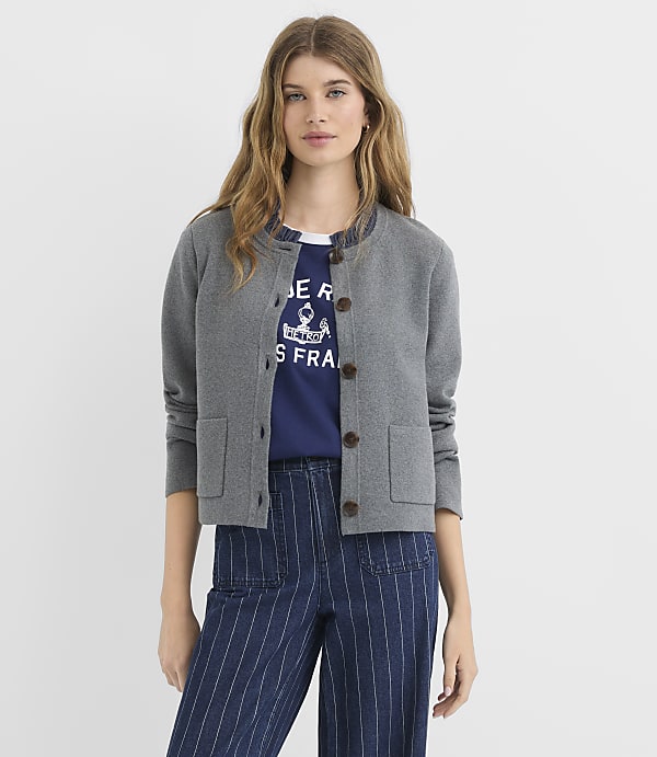 A woman in a grey cardigan and striped pants stands against a plain white background.