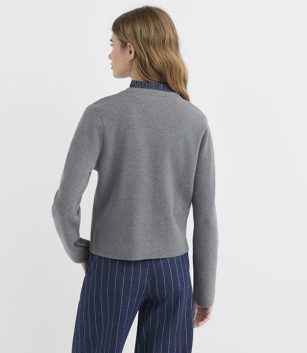 A woman in a gray cardigan and striped pants stands against a plain white background.