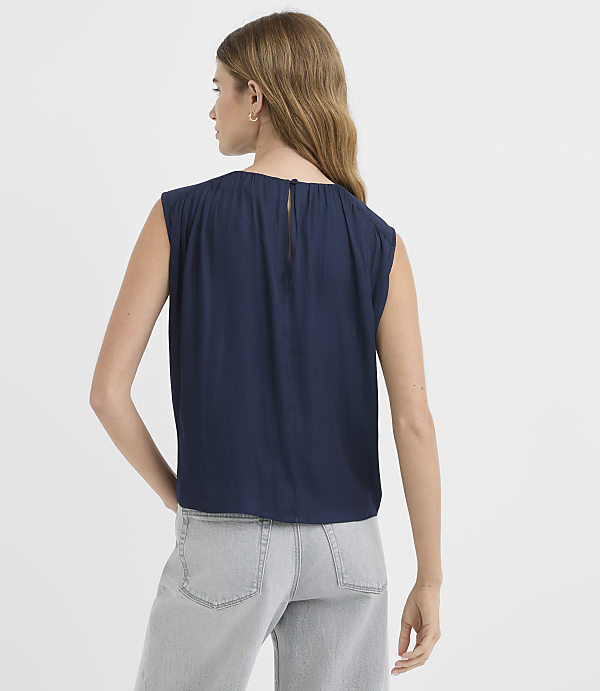 A woman in a navy blue top and light gray jeans stands against a plain white background.
