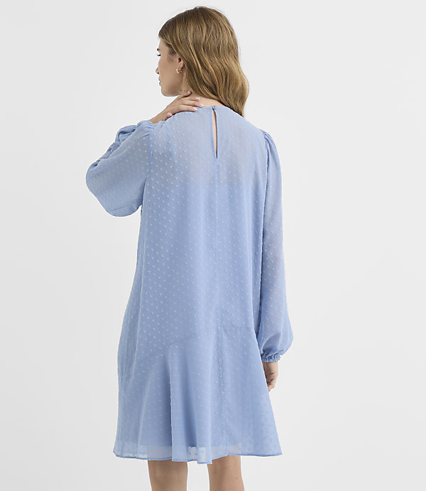 A woman in a light blue, textured dress stands against a plain white background.