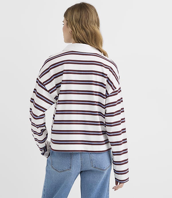 A young woman in a striped shirt and jeans stands against a plain white background.