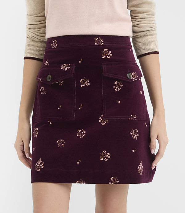 A burgundy corduroy skirt with a floral pattern and two front pockets is worn by a person against a plain white background.