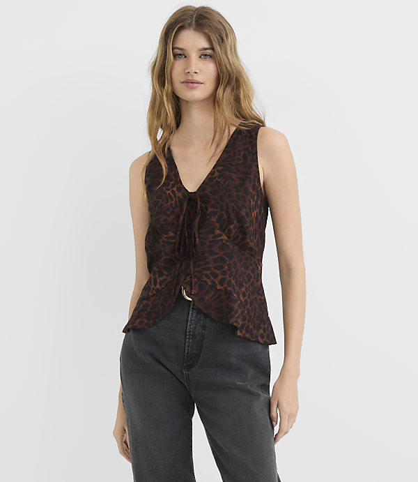 A woman in a leopard print top and dark jeans stands against a plain white background.