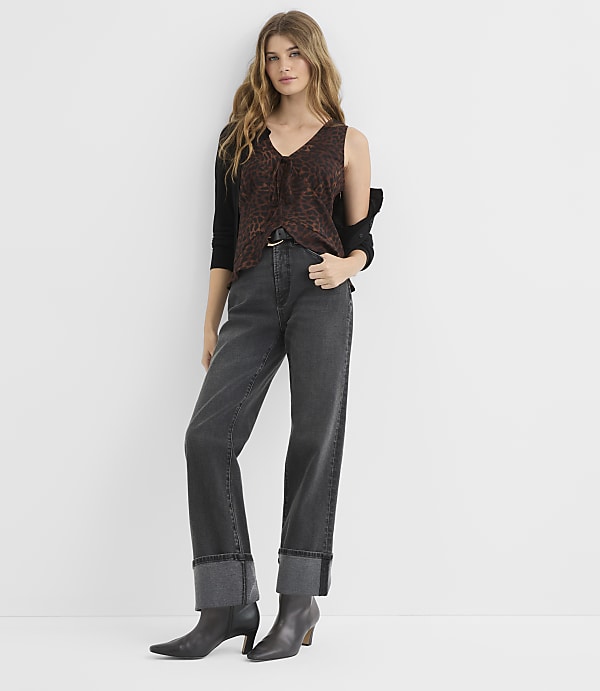 A woman in a leopard print top and dark jeans stands against a plain white background.
