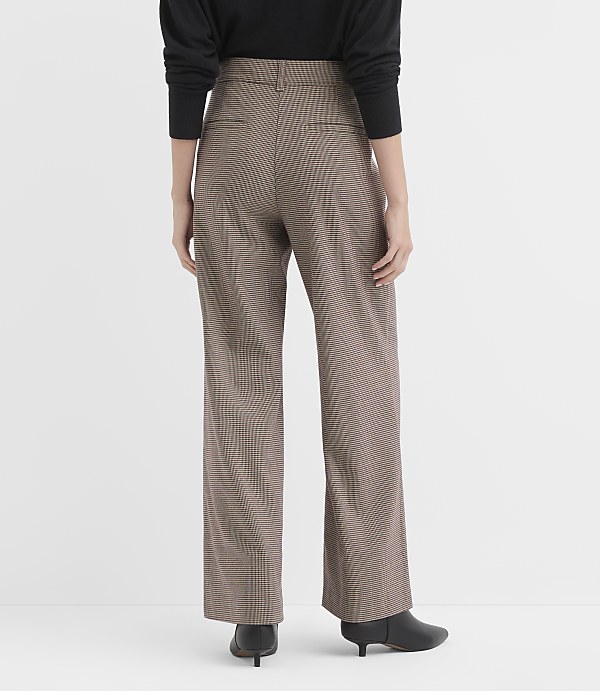 A person wearing brown plaid wide-leg pants and black heeled boots stands against a plain white background.