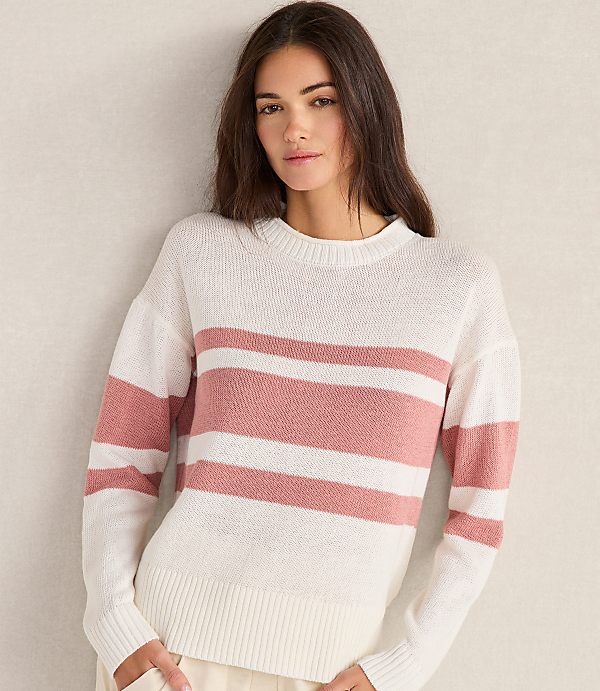 A woman in a striped sweater stands against a plain, light-colored wall.