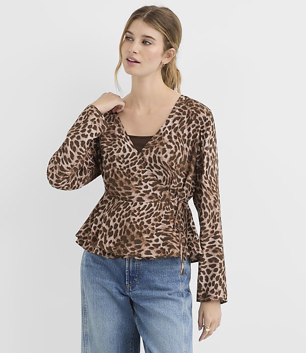 A woman in a leopard-print wrap top and blue jeans stands against a plain white background.