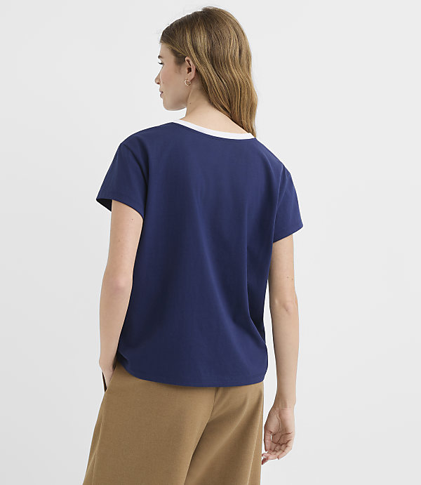 A woman in a navy t-shirt and brown pants stands against a plain white background.
