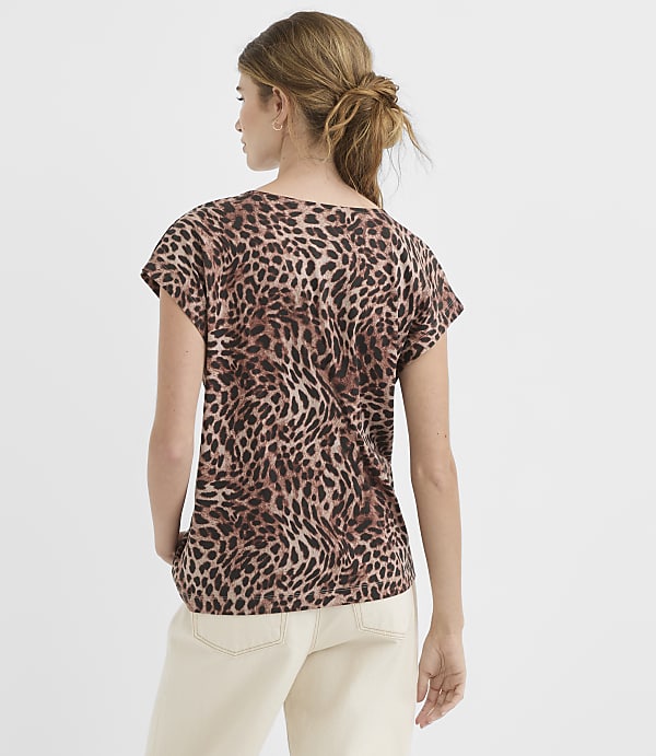 A woman in a leopard print t-shirt and cream pants stands against a plain white background.