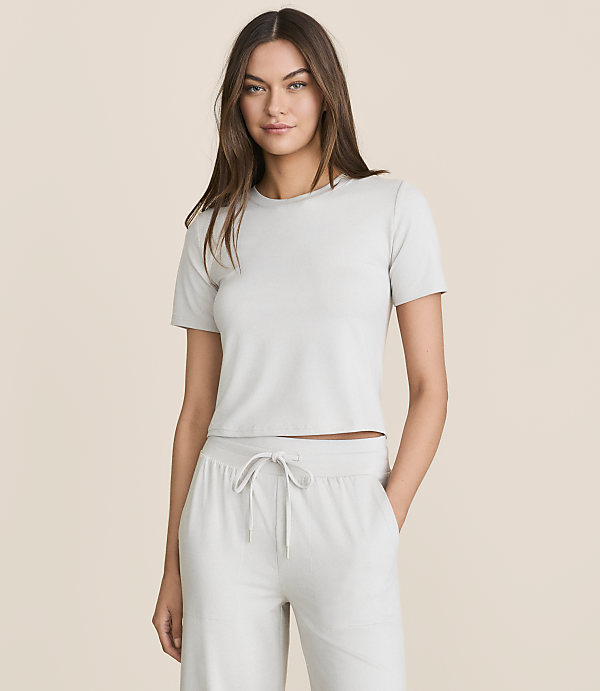 A woman in a light gray cropped t-shirt and matching drawstring pants stands against a plain, light beige background.