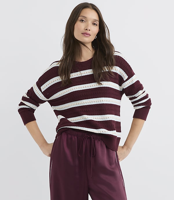 A woman in a striped sweater and satin pants stands against a plain white background.