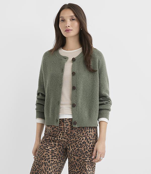 A woman in a green cardigan and leopard print pants stands against a plain white background.