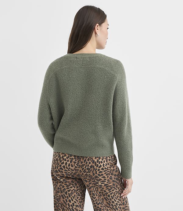 A woman in a green sweater and leopard print pants stands against a plain white background.