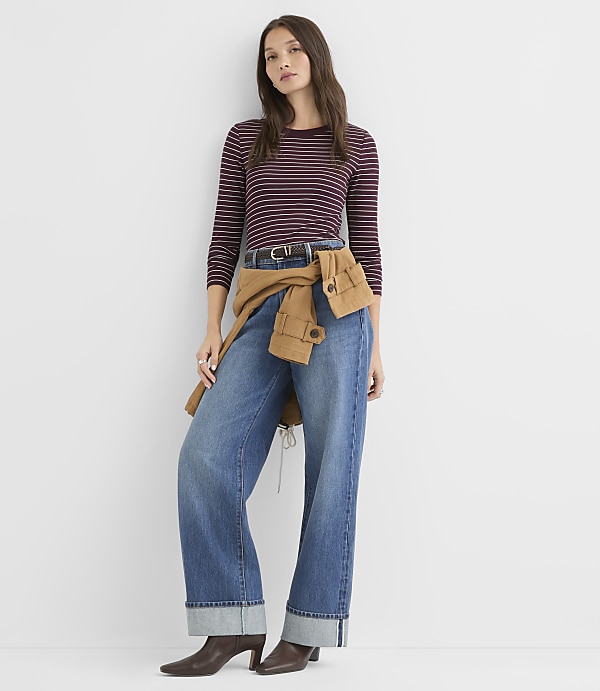 A woman in a striped shirt and wide-leg jeans stands against a plain white background.