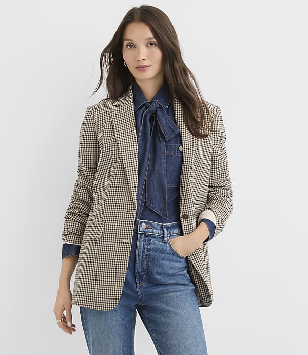 A woman in a patterned blazer and denim shirt stands against a plain white background.