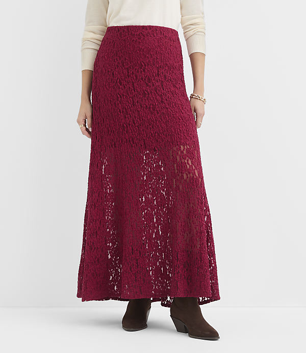 A woman in a cream sweater and a long, flowing burgundy lace skirt stands against a plain white background.