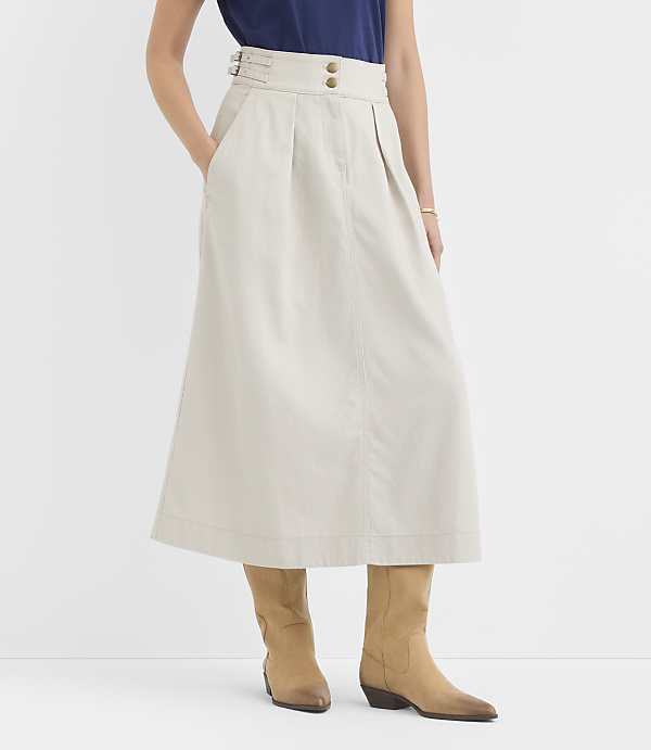 A person stands in a light-colored midi skirt and tan boots against a plain white background.