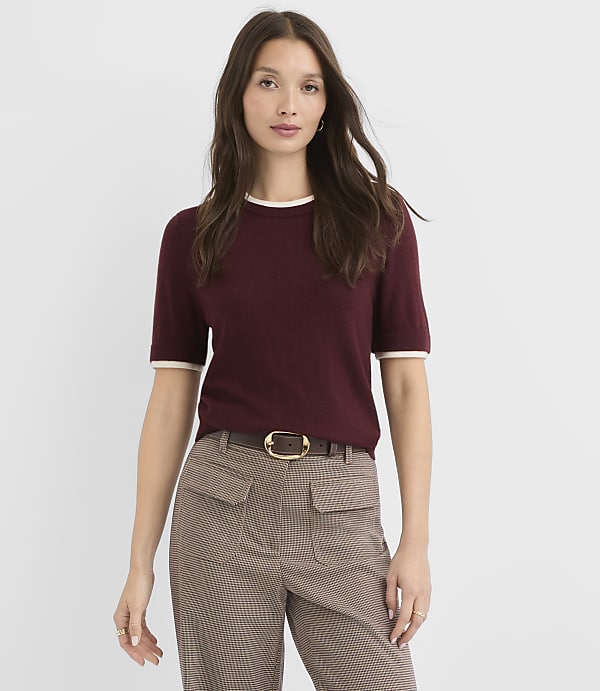 A woman in a maroon sweater and plaid pants stands against a plain white background.