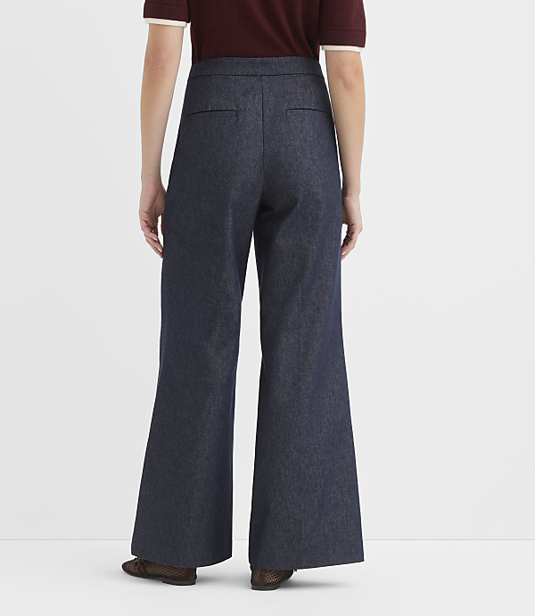 A person wearing dark wash wide-leg jeans and a maroon polo shirt stands against a plain white background.