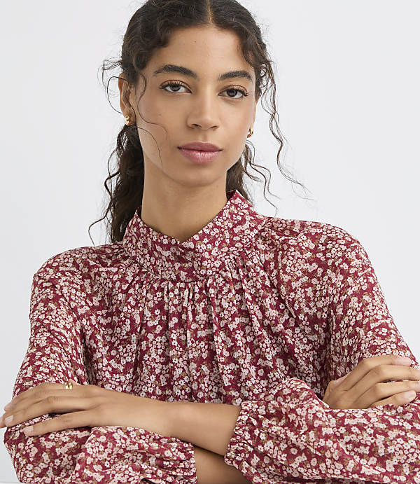 A woman with dark curly hair and a floral print blouse is posed against a plain white background.