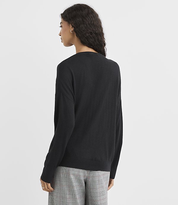 A woman in a black sweater and plaid pants stands against a plain white background.