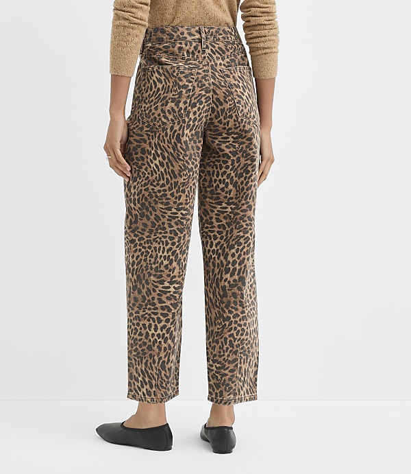 A person wearing leopard-print pants and a brown sweater stands against a plain white background.