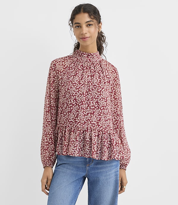 A woman in a floral print blouse and jeans stands against a plain white background.