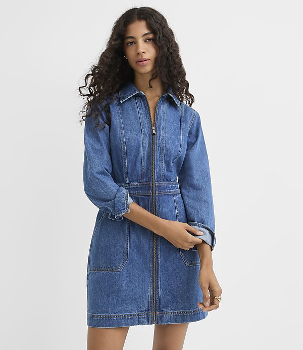 A woman in a denim dress stands against a plain white background.
