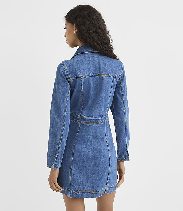 A woman in a denim dress stands against a plain white background.