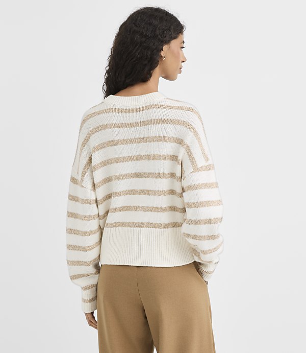 A woman in a cream and gold striped sweater stands against a plain white background.