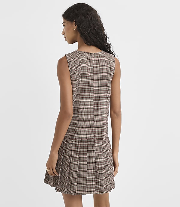 A woman in a plaid dress stands against a plain white background.