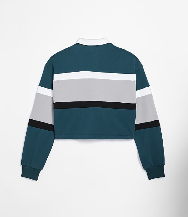 A cropped, long-sleeved rugby shirt with teal, white, gray, and black stripes is displayed against a plain white background.