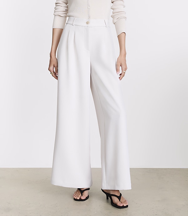 A person stands in wide-leg white pants and black heels against a plain white background.