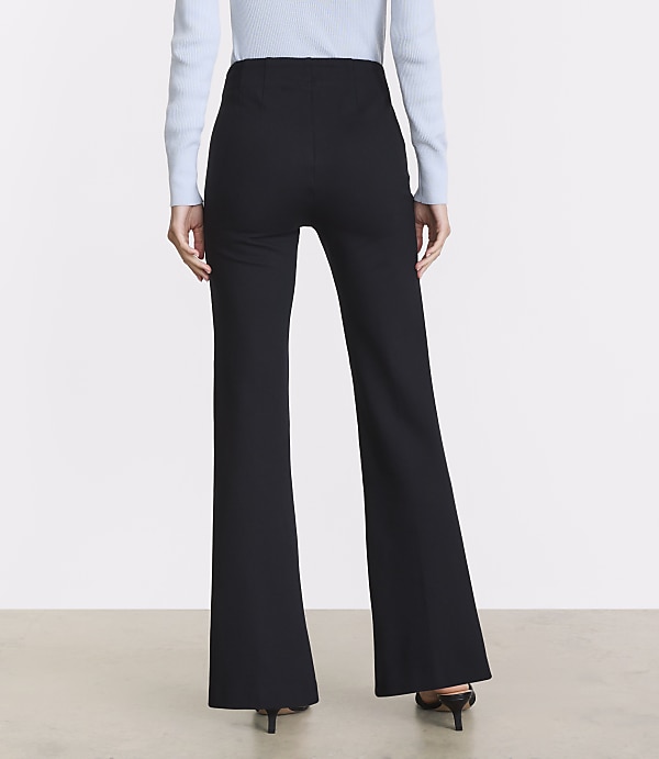 A person wearing black flared pants and a light blue sweater stands against a plain, light-colored background.