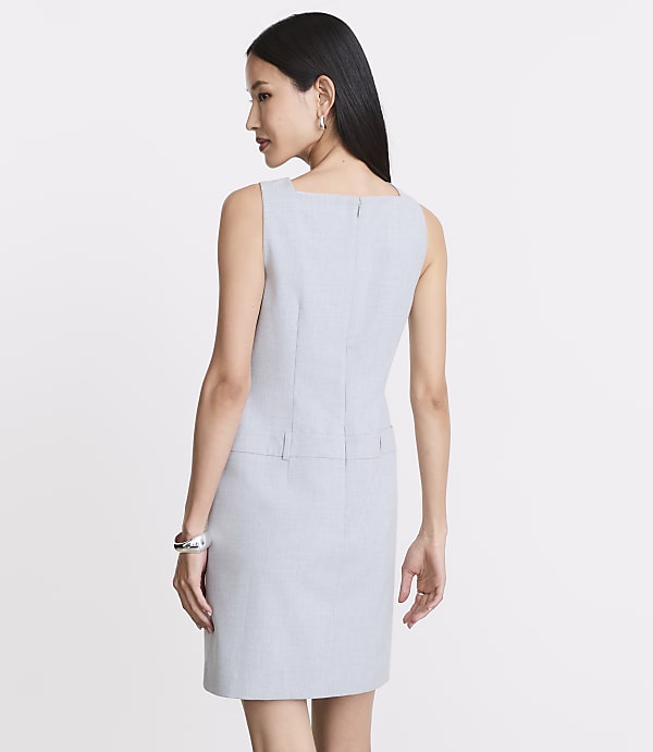 A woman in a light gray dress stands against a plain white background.