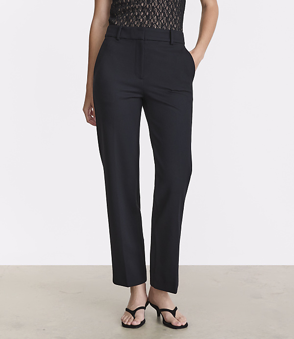 A person stands in black trousers and a lace top against a plain white background.