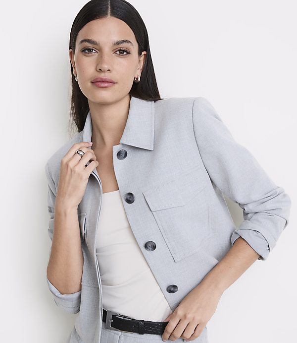 A woman in a light blue jacket and white top stands against a plain white background.