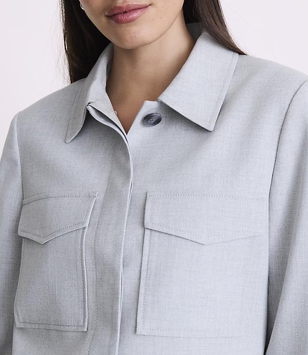 A woman in a light blue collared shirt with two chest pockets is shown from the chest up against a plain background.