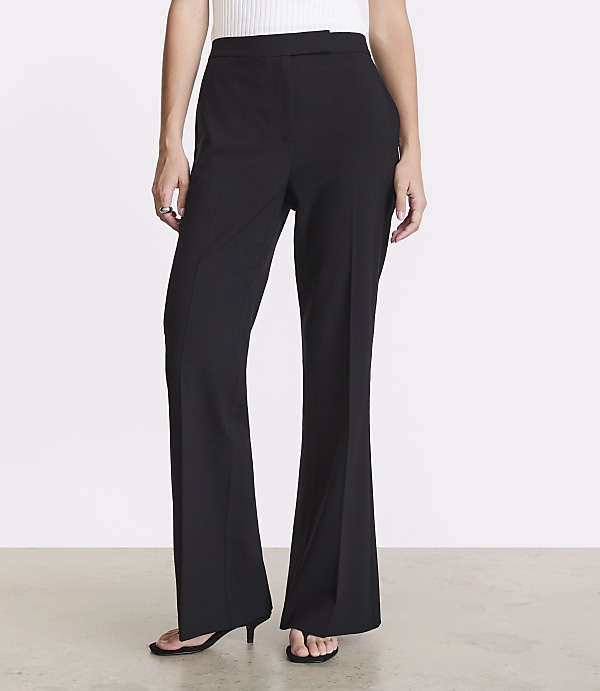 A person stands in black flared pants and a white top against a plain white background.