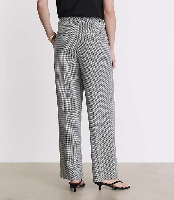 A person wearing black and white checkered pants and black kitten heels stands against a plain white background.