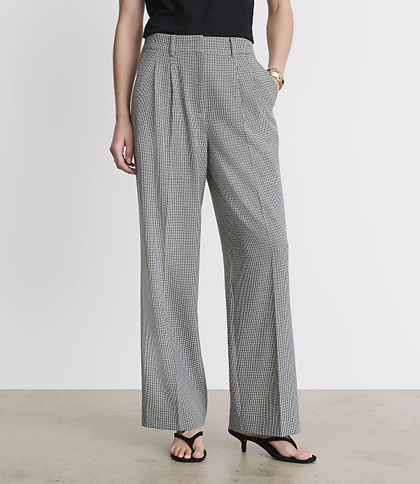 A person stands in front of a plain white background, wearing wide-leg, black and white patterned pants and black sandals.